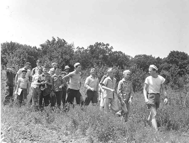 A black-and-white photo of boys marching in a line through a field.